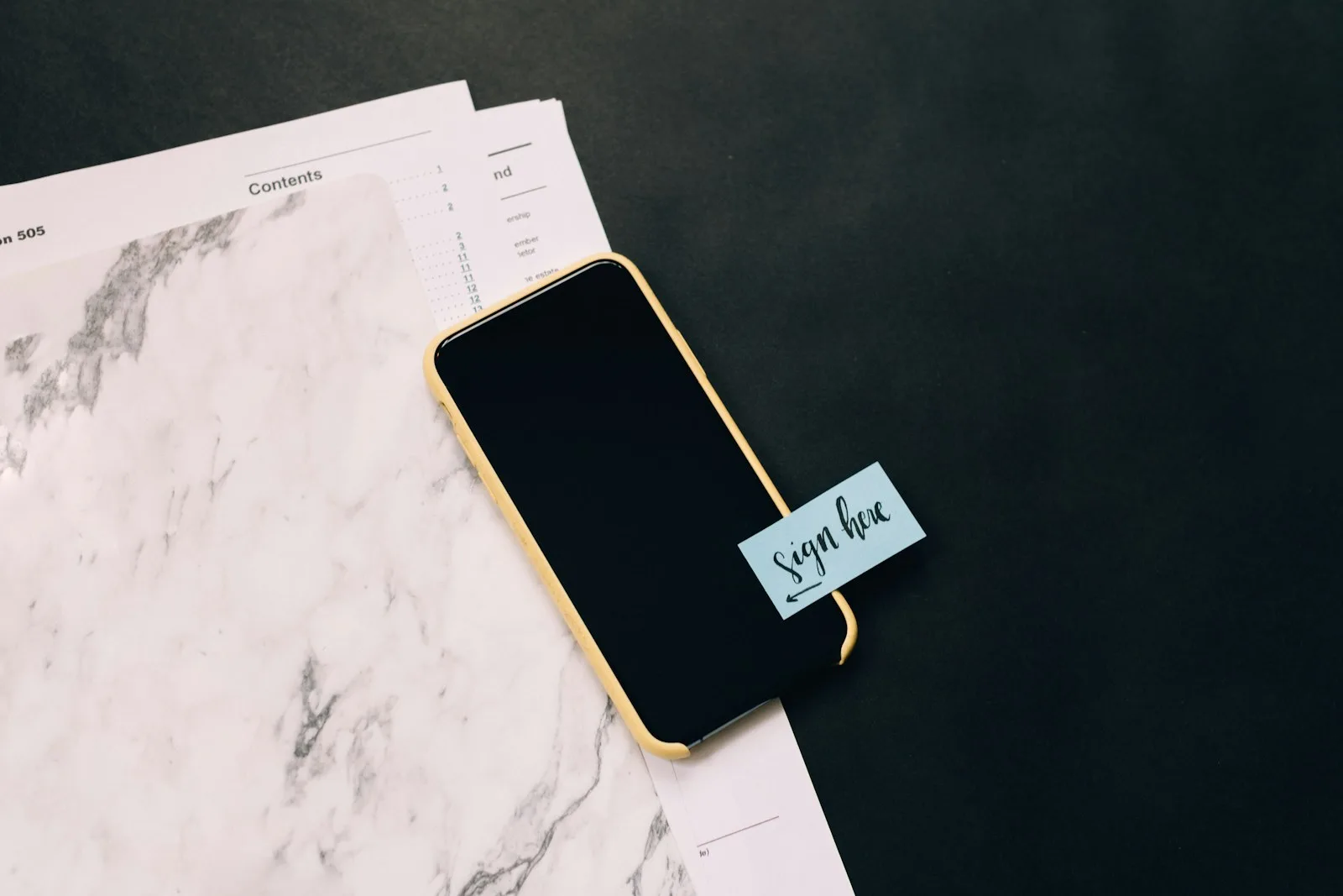 Image of a mobile phone with a paper mentioning “sign here”